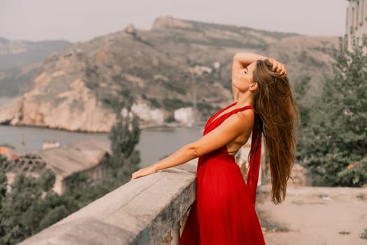 Woman red dress. Summer lifestyle of a happy woman posing near a fence with balusters over the sea