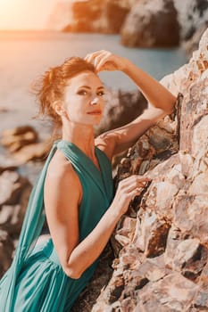 Woman green dress sea. Woman in a long mint dress posing on a beach with rocks on sunny day. Girl on the nature on blue sky background