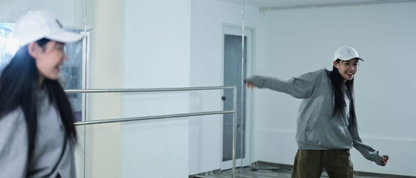 Shot of expressive young woman in caps practicing break dance in studio.