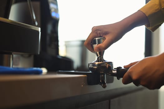 Cropped shot of barista hand tamping freshly ground coffee beans in a portafilter.