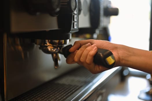 Cropped shot of barista using coffee machine, making espresso for client in a trendy cafe.