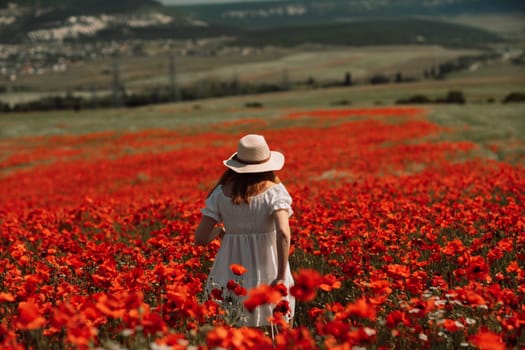 Field poppies woman. Happy woman in a white dress and hat stand with her back a blooming field of poppy. Field of blooming poppies