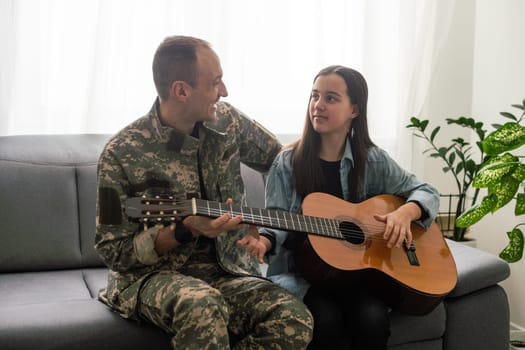 The veteran came back from army. A man in uniform with his daughter. The veteran is playing the guitar. High quality photo