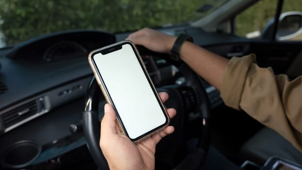 Cropped shot of man sitting behind wheel of a car and using smartphone. Closeup view.