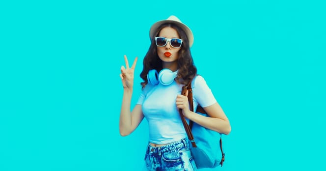 Portrait of modern happy young woman listening to music with headphones on blue studio background