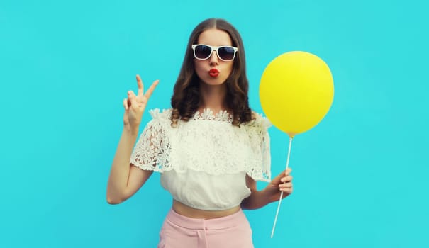 Portrait of happy young woman with yellow balloon on blue studio background