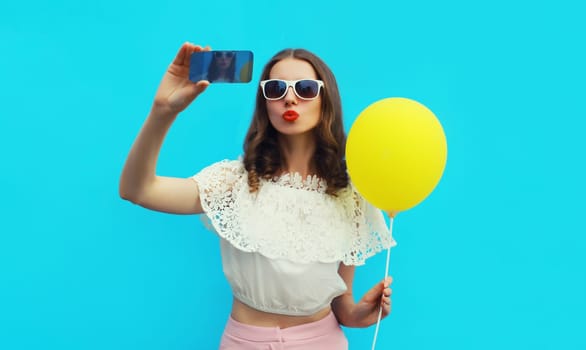 Portrait of beautiful young woman 20s taking selfie with cellphone and blowing her lips sends kiss on blue studio background