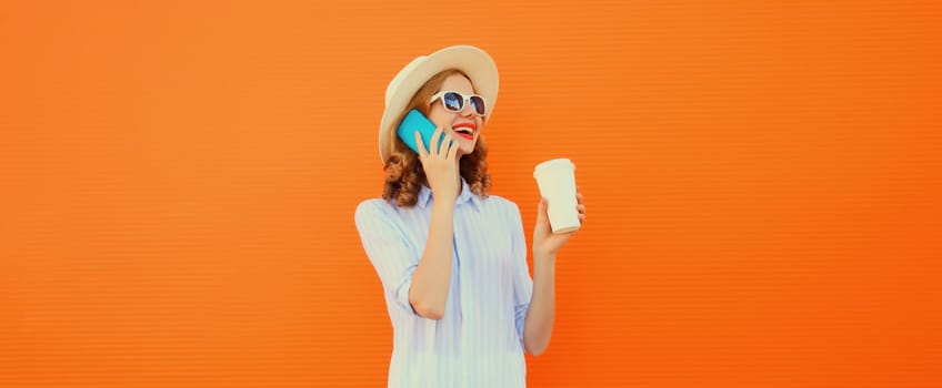 Happy cheerful smiling young woman calling on mobile phone with cup of coffee wearing summer straw hat on orange background