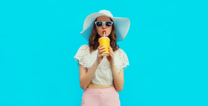 Portrait of beautiful caucasian young woman model with cup of coffee or fresh juice wearing white summer straw hat on studio blue background