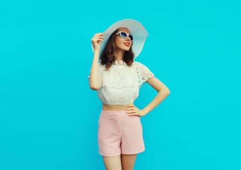 Beautiful caucasian young woman model posing wearing white summer straw hat on blue studio background