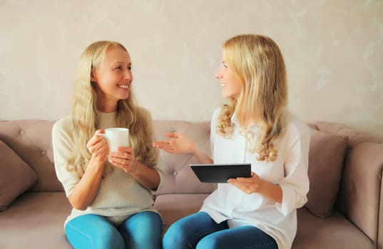 Happy smiling caucasian middle aged mother and adult daughter, women talking and looking at each other together sitting on couch at home