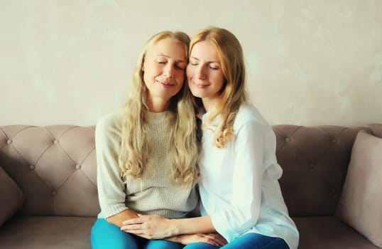 Portrait of happy smiling caucasian middle aged mother hugging her adult daughter together sitting on couch at home