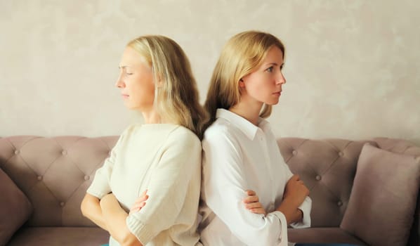 Upset offended caucasian middle aged mother or sister and adult daughter together sitting on couch at home