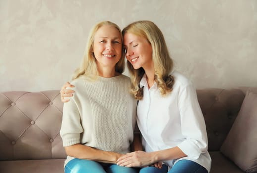 Portrait of happy smiling caucasian middle aged mother hugging her adult daughter together sitting on couch at home