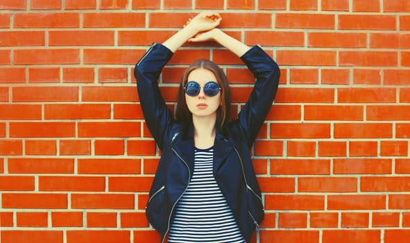 Portrait of stylish young woman model wearing black leather jacket in rock style on city street on brick wall background