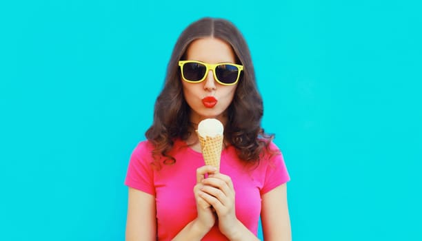 Summer portrait of happy young woman eating ice cream wearing sunglasses on blue background