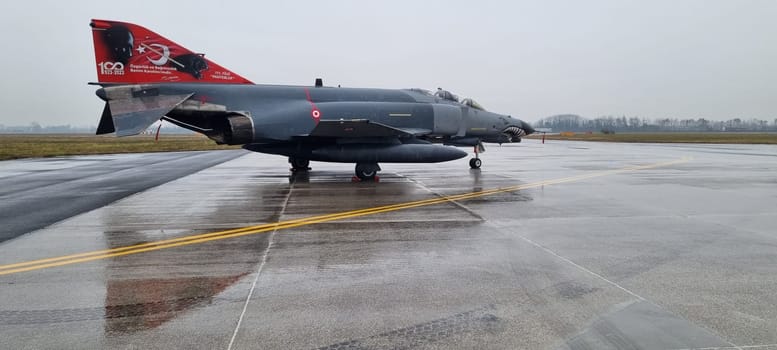 Turkish F-4 Phantom fighter jet parked on a rainy day, its formidable presence underscored by the relentless downpour, capturing a moment of quiet strength.