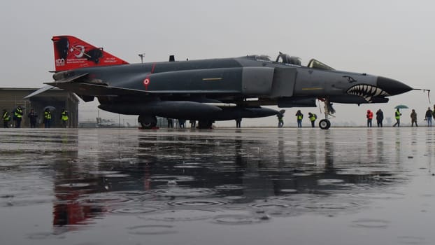 Turkish Phantom fighter jet, parked under the rain, casts its reflection on the water-saturated ground, merging the power of military aviation with the tranquility of nature. Copy space.