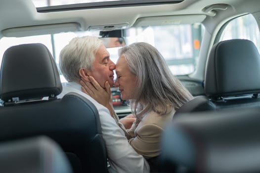 Mature Caucasian couple sitting in a new car and rejoicing at the purchase
