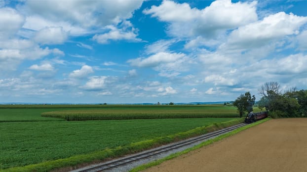 Railroad Tracks Curve Gently Through A Lush Agricultural Landscape With Fields Of Various Shades Of Green Under A Wide Sky With Broken Clouds.