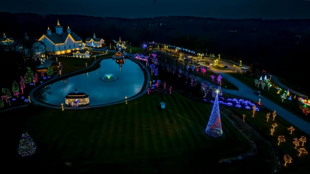 Aerial View Of A Reflective Pond Amidst A Serpentine Pathway Surrounded By Buildings And Trees Adorned With Vibrant Holiday Lights At Night.