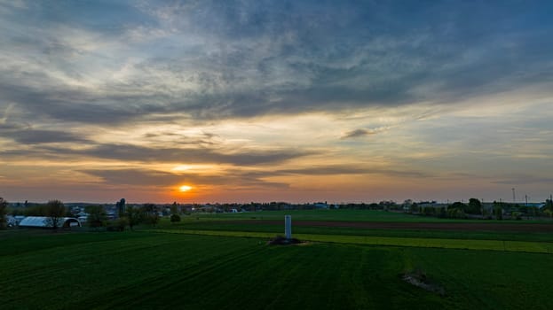 Aerial View of Dramatic Sunset Casting A Warm Glow Over A Rural Landscape With Silhouetted Trees And Buildings Under A Cloud-Streaked Sky.