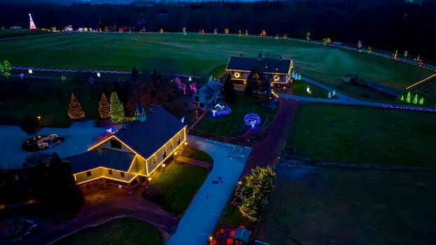 Aerial View Of An Evening Scene With Illuminated Buildings And A Large Field Surrounded By Christmas Trees And Light Decorations.