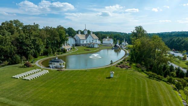Aerial View Capturing A Series Of White Buildings With Orthodox Christian Architectural Features, Set Beside A Symmetrical Pond With Fountains, Flanked By Green Trees And Manicured Lawns.