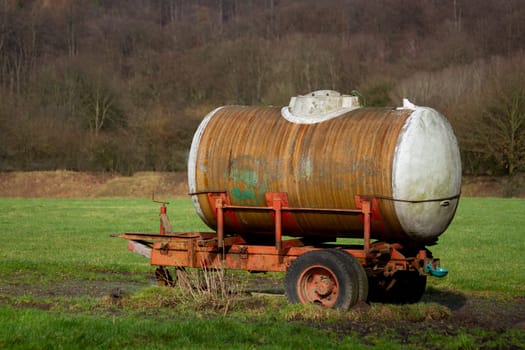 Retro tank trailer with wooden wheels parked in rural grassland. High quality
