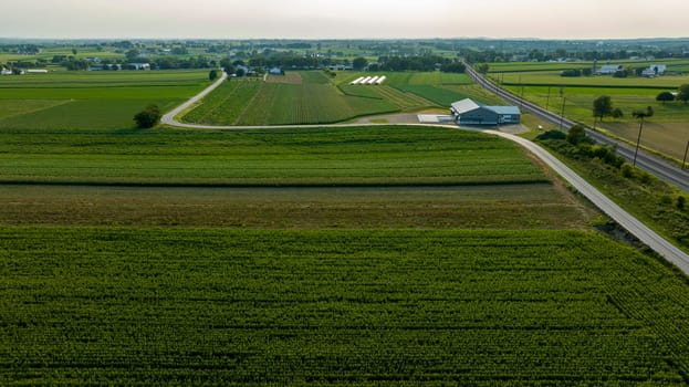 High Angle View Showcasing A Stretch Of Road And Railroad Tracks Cutting Through A Lush Tapestry Of Agricultural Fields With Farm Buildings In The Distance.