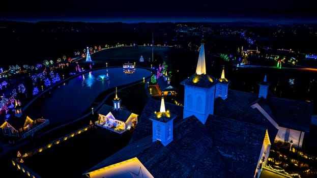 Overhead View Of A Complex With Ornate Buildings And A Pond, Surrounded By A Colorful Array Of Christmas Lights At Night.