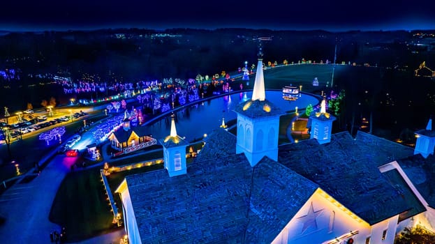 Overhead View Of A Complex With Ornate Buildings And A Pond, Surrounded By A Colorful Array Of Christmas Lights At Night.