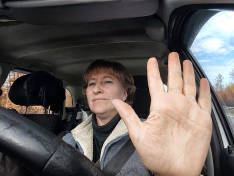 Funny cute blonde girl or a middle-aged woman driving a car in summer, autumn, spring day. A female driver on a solo trip