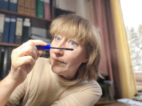 Portrait of a middle-aged woman doing eye makeup. Selfie portrait of lady who is businesswoman, accountant, manager, freelancer doing morning makeup at office on working place