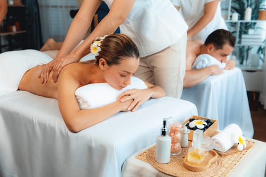 Caucasian couple customer enjoying relaxing anti-stress spa massage and pampering with beauty skin recreation leisure in day light ambient salon spa at luxury resort or hotel. Quiescent