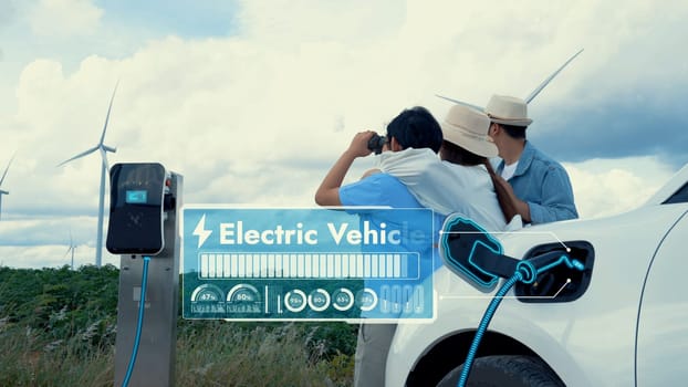 Modern family travel and nature with eco-friendly EV car concept, display digital battery recharging status hologram using renewable energy from wind turbine for future energy sustainability. Peruse
