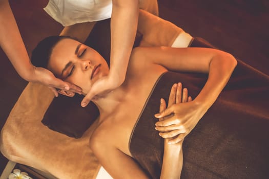 Caucasian woman enjoying relaxing anti-stress head massage and pampering facial beauty skin recreation leisure in warm candle lighting ambient salon spa in luxury resort or hotel. Quiescent