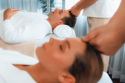 Caucasian couple enjoying relaxing anti-stress head massage and pampering facial beauty skin recreation leisure in dayspa modern light ambient at luxury resort or hotel spa salon. Quiescent