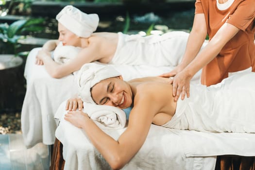 A portrait of two young attractive woman lie on bed during having back massage by a professional masseur at outdoor surrounded by peaceful natural environment. Healthy and beauty concept. Tranquility.