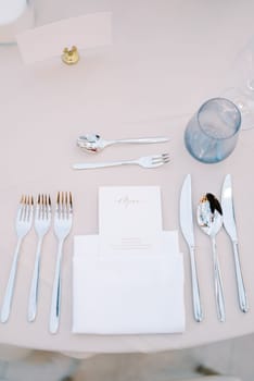 Personalized invitation lies in a white napkin on the table next to the cutlery, opposite a blank card on a stand. High quality photo