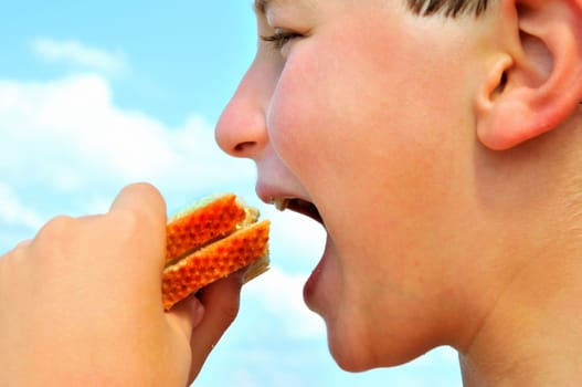 A boy bites a sandwich against a background of blue sky with white clouds