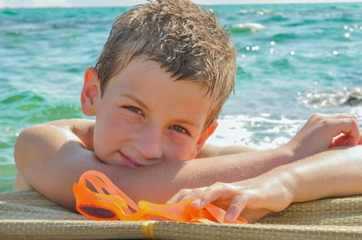 The boy swam to the shore and rests holding on to a rock and holding his swimming goggles