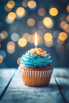 A single cupcake with blue icing and a lit candle against a bokeh background