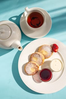 Start your day with a delightful breakfast of cottage cheese pancakes topped with indulgent sour cream and sweet jam, accompanied by a warm cup of tea for a perfect morning treat.