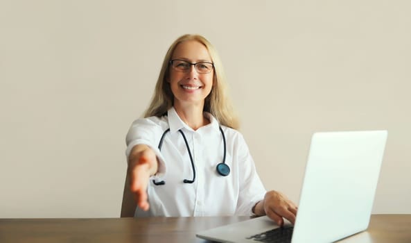 Caucasian middle-aged woman doctor working with laptop computer while sitting at desk in medical clinic office