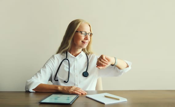 Caucasian middle-aged woman doctor with stethoscope, paper documents and digital tablet computer sitting at desk in clinic office