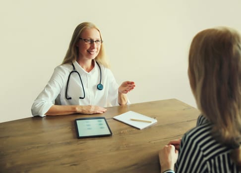 Patient at doctor's appointment. Caucasian middle-aged woman doctor therapist talking to the girl prescribes medications while sitting at table in clinic office
