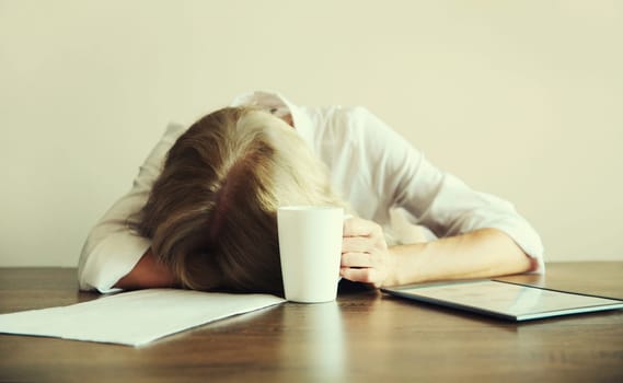 Tired overworked sleepy woman employee with headache holding cup asking to drink extra coffee while working with digital tablet computer sitting at desk at home or office in morning