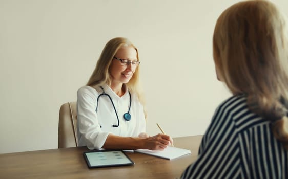 Patient at doctor's appointment. Caucasian middle-aged woman doctor therapist talking to the girl prescribes medications while sitting at table in clinic office