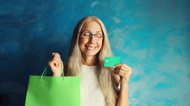 Portrait of happy smiling caucasian middle aged woman holding plastic credit bank card with shopping bags on studio background